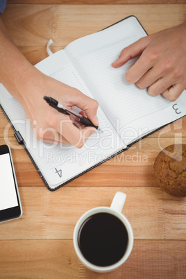 Man writing on diary with muffin and coffee at desk