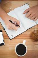 Man writing on diary with muffin and coffee at desk