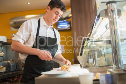 Male worker cutting sandwich at display cabinet