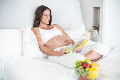 Happy woman reading novel with Granny Smith on bed