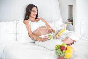 Happy woman reading novel with Granny Smith on bed