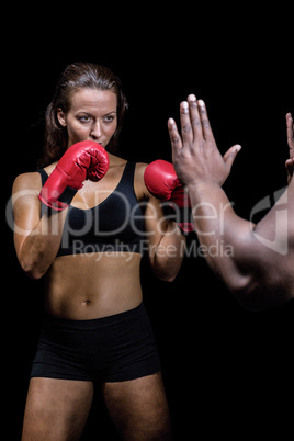 Female boxer with fighting stance against trainer hand