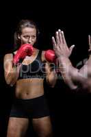 Female boxer with fighting stance against trainer hand