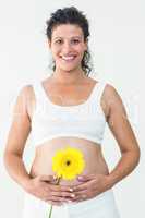 Smiling pregnant woman touching her stomach while holding yellow