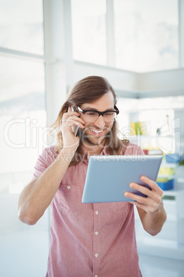 Hipster using mobile phone while looking at digital tablet