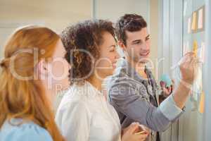 Businessman writing on glass wall as female colleagues looking a