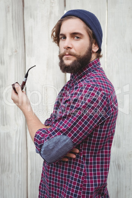 Side view of hipster holding smoking pipe