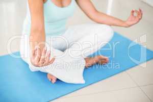Pregnant woman sitting in lotus pose on exercise mat