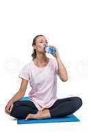 Fit woman drinking water while sitting on mat