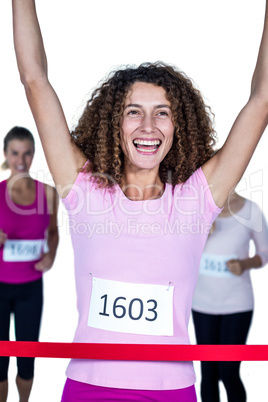 Smiling winner female athlete crossing finish line with arms rai
