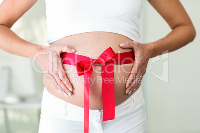 Midsection of woman holding belly with ribbon