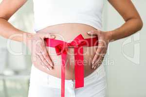 Midsection of woman holding belly with ribbon