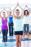 Happy and fit women with hands joined overhead in fitness studio