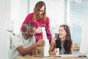 Smiling business people holding coffee cups at computer desk