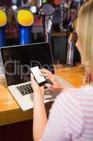 Woman with laptop using mobile phone at table