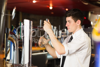 Barkeeper holding glass in front of beer dispenser at bar