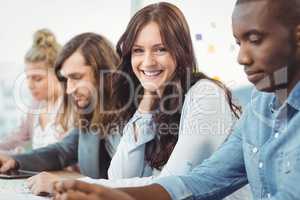 Portrait of smiling woman sitting at desk with coworkers