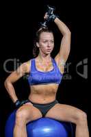 Woman exercising with dumbbell while sitting on ball