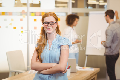 Confident businesswoman with arm crossed with colleagues in back