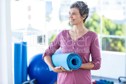 Happy thoughtful mature woman with yoga mat