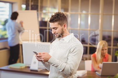 Businessman texting on phone with colleagues working in office