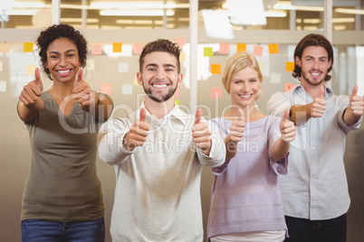 Portrait of smiling business team gesturing thumps up in office