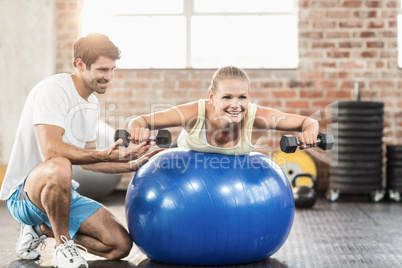 Male trainer helping young woman with the dumbbells