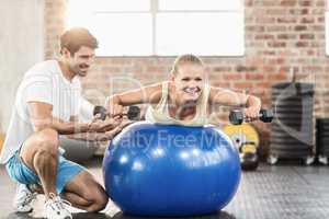 Male trainer helping young woman with the dumbbells