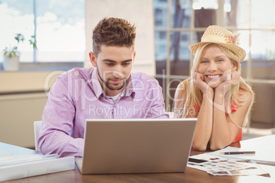 Business woman wearing hat sitting by male colleague