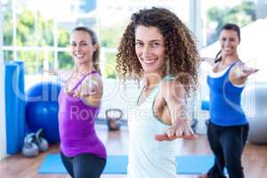 Fit women doing warrior II pose in fitness studio