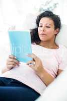 Pregnant woman reading book on sofa