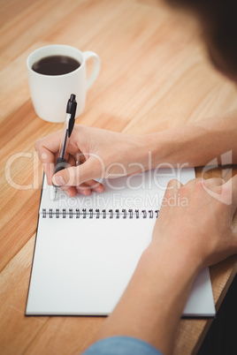 Hipster writing on spiral notebook at desk in office