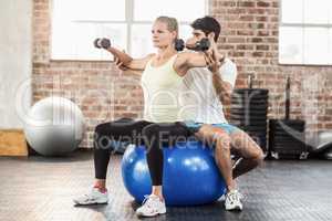 Male trainer helping young woman with the dumbbells