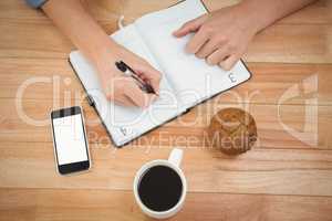 Hipster writing on diary with muffin and coffee at desk