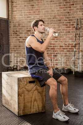 Man sitting on plyo box and drinking water
