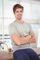 Hipster with arms crossed smiling while sitting at desk