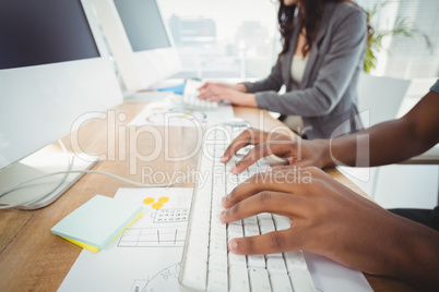 Cropped hands typing on keyboard at computer desk with coworker