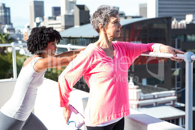 Mature woman stretching with female friend by railing