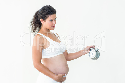 Pregnant woman looking away while holding alarm clock