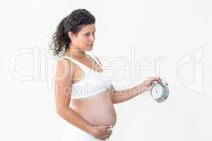 Pregnant woman looking away while holding alarm clock