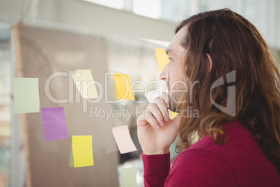 Thoughtful man looking at adhesive notes stuck on glass