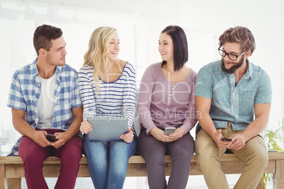 Smiling business people holding electronic gadgets while sitting