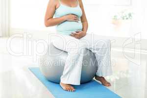 Pregnant woman sitting on exercise ball touching her belly