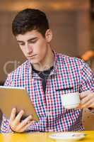 Young man using digital tablet while holding coffee cup