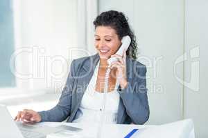 Pregnant businesswoman talking on phone while working on laptop