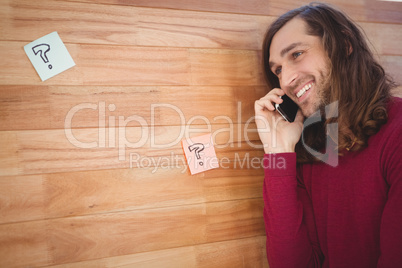 Happy man using mobile phone leaning on wooden wall