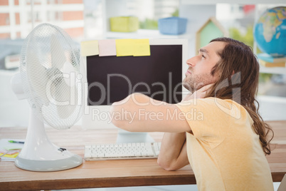 Tired hipster sitting by electric fan on desk