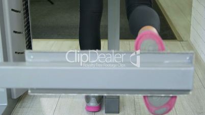 Woman working out on standing leg curl machine in fitness club closeup