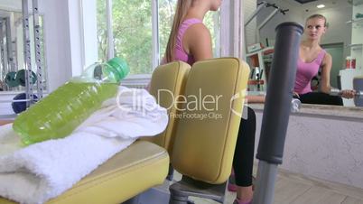Young woman training in fitness club doing dumbbell exercise in front of mirror