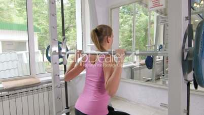 Fit young woman working out in fitness club doing exercise with barbell